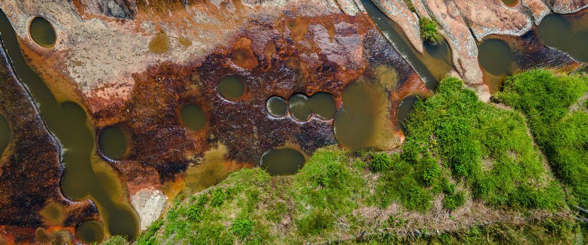 A rocky landscape with multiple circular ponds and patches of green vegetation.