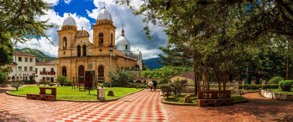 A historic church with two domes, a red-tiled courtyard, and surrounding greenery.