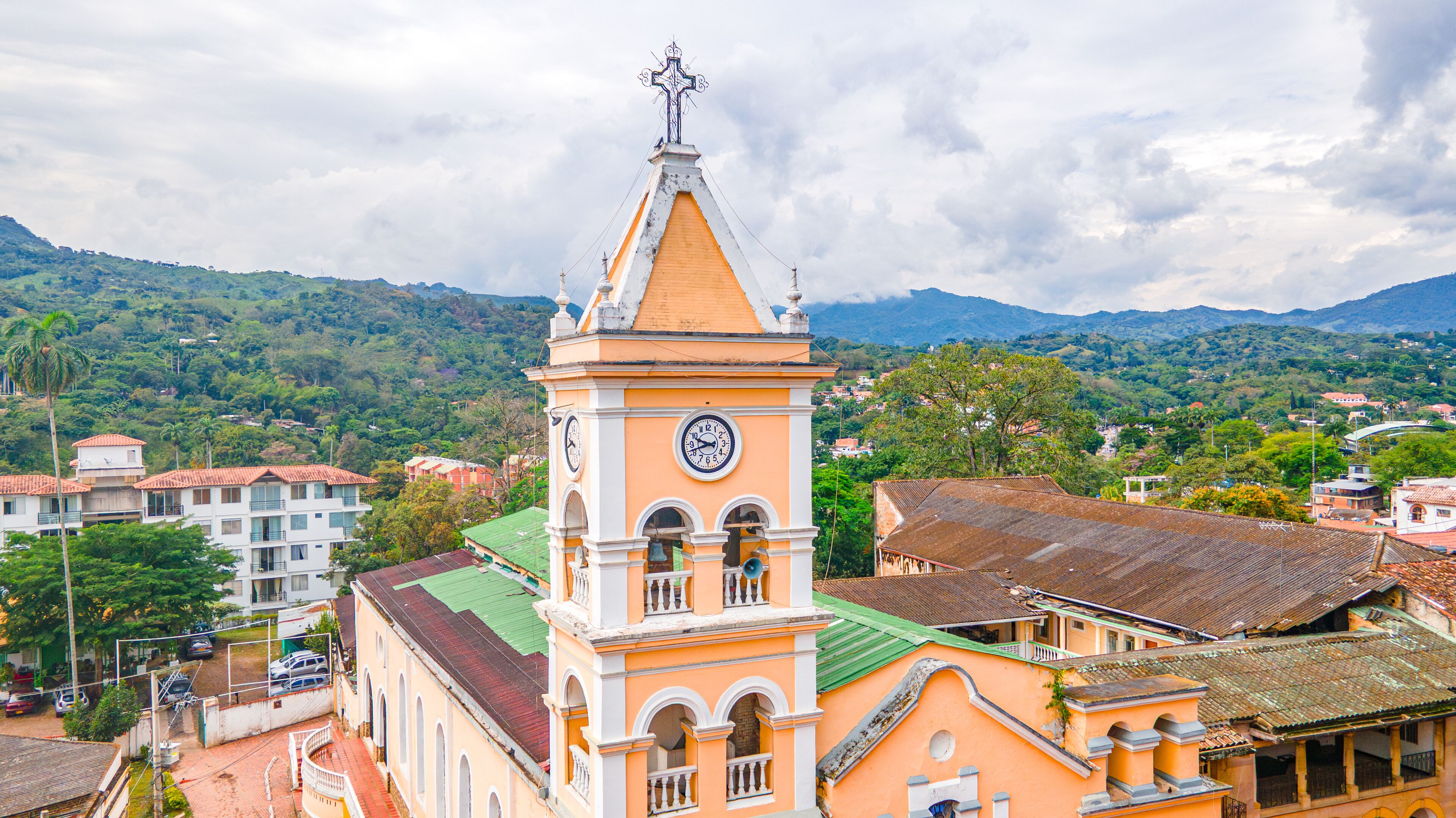 A church with a clock tower, surrounded by residential buildings and lush green hills.