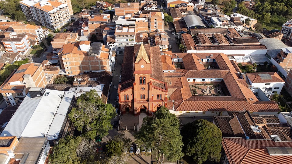 An aerial view of a densely packed urban area with a prominent red-brick church with a clock tower, surrounded by residential buildings with red-tiled roofs.