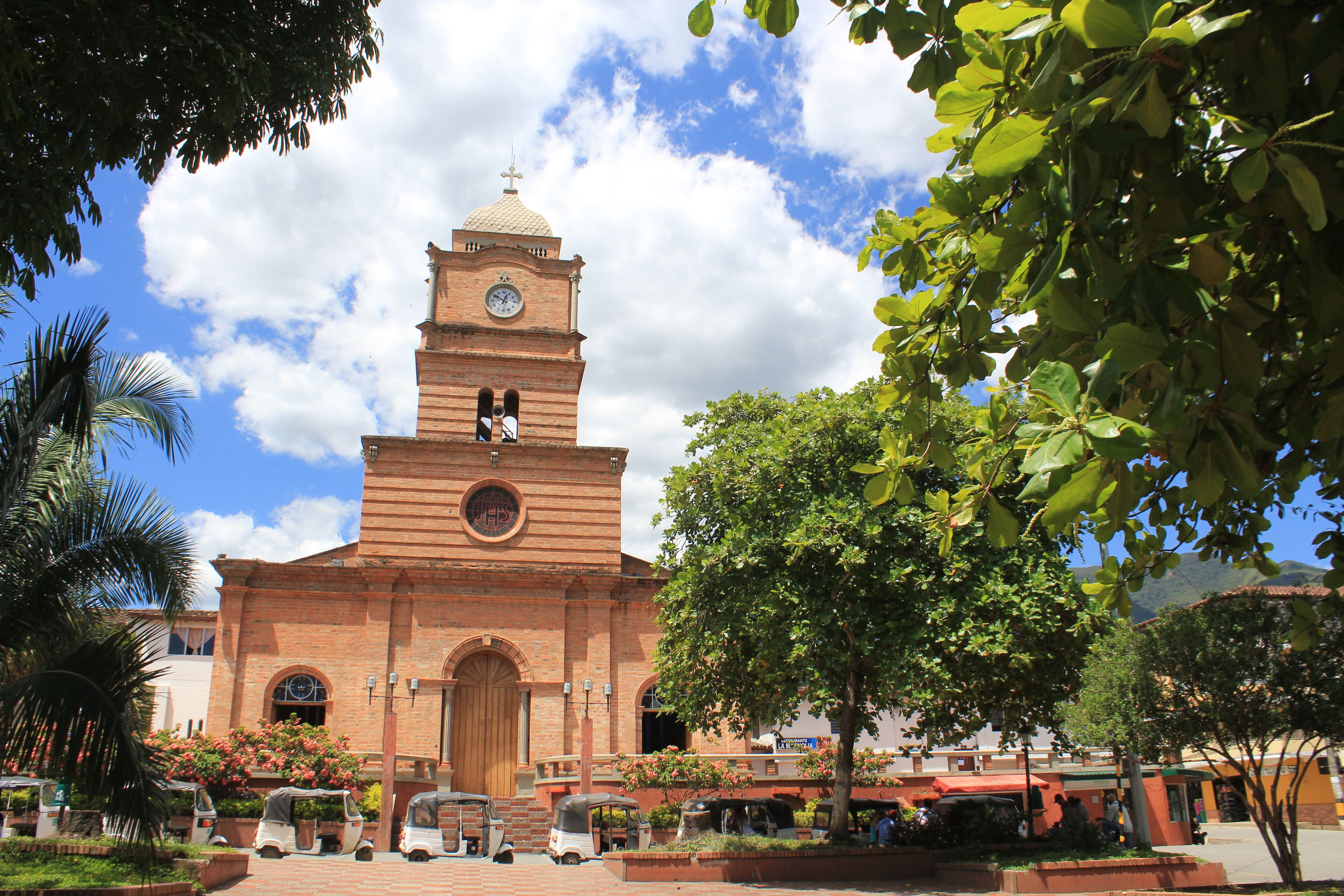A historic church with a clock tower, surrounded by lush greenery and palm trees.