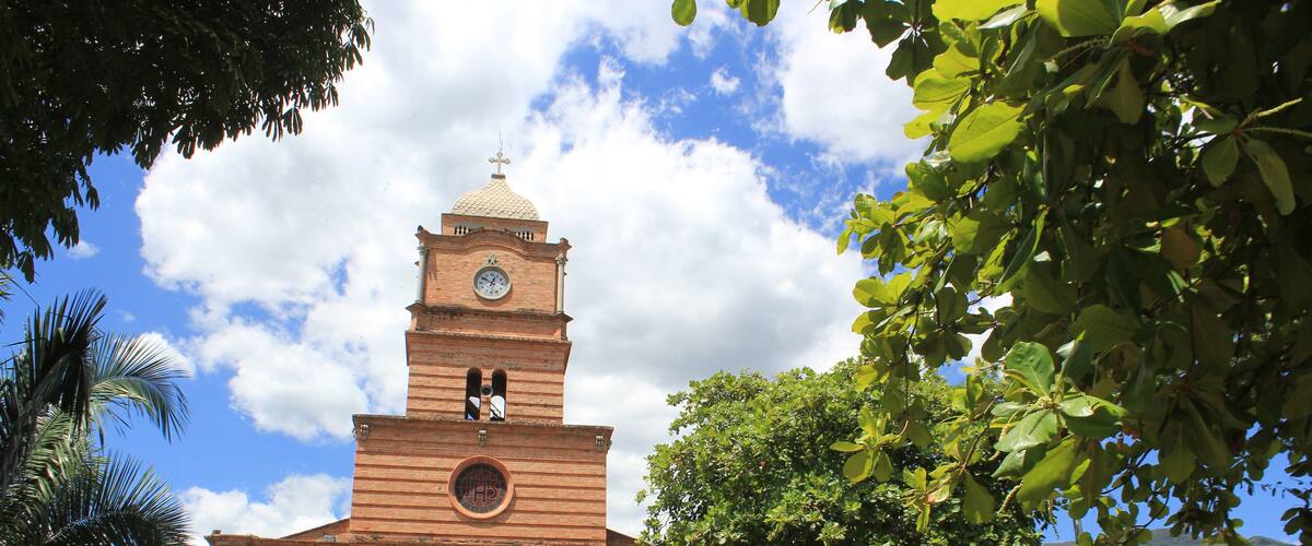 A historic church with a clock tower, surrounded by lush greenery and palm trees.