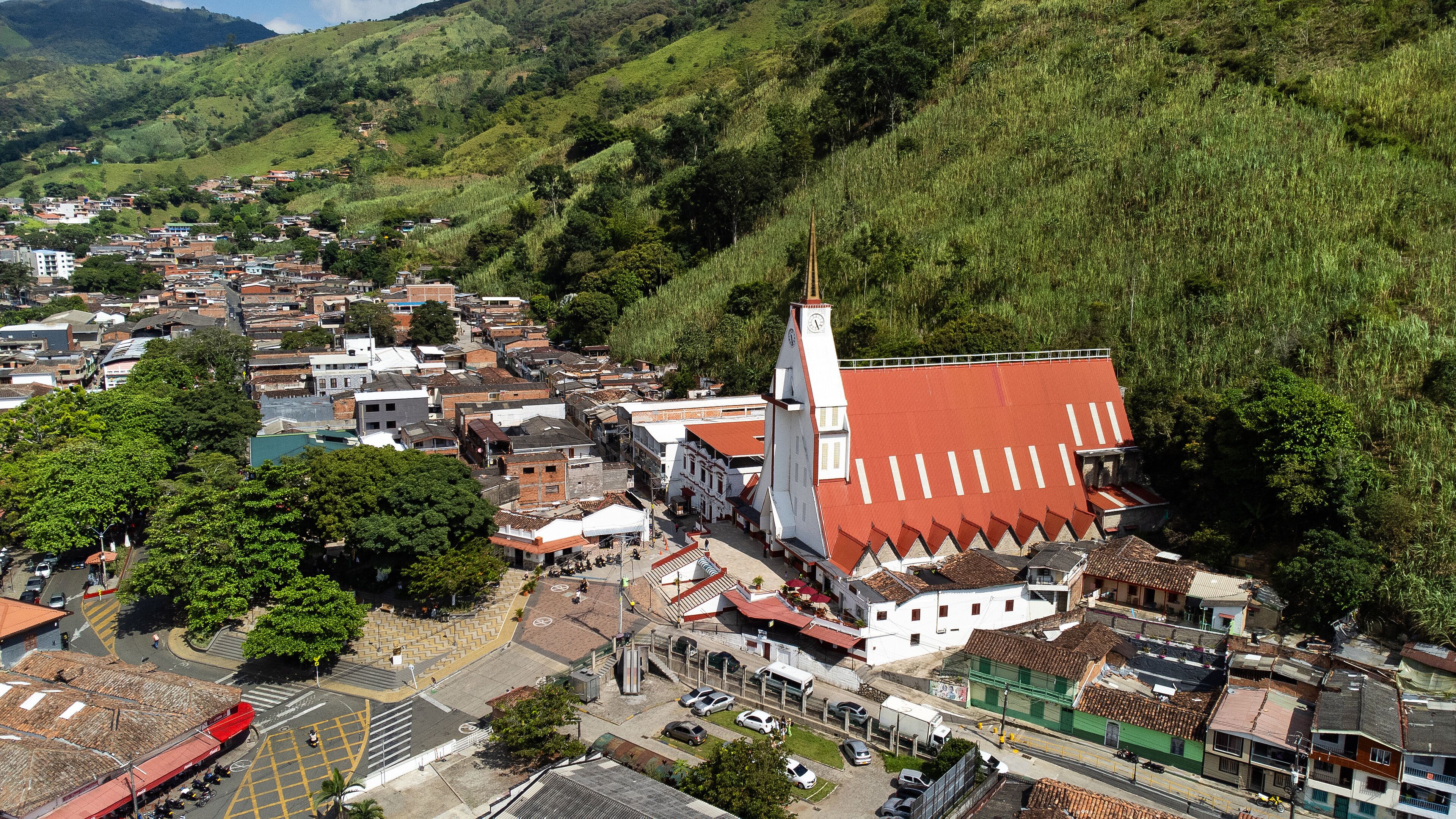 A town with a prominent church featuring a clock tower, surrounded by lush green hills and a mix of traditional and modern buildings.