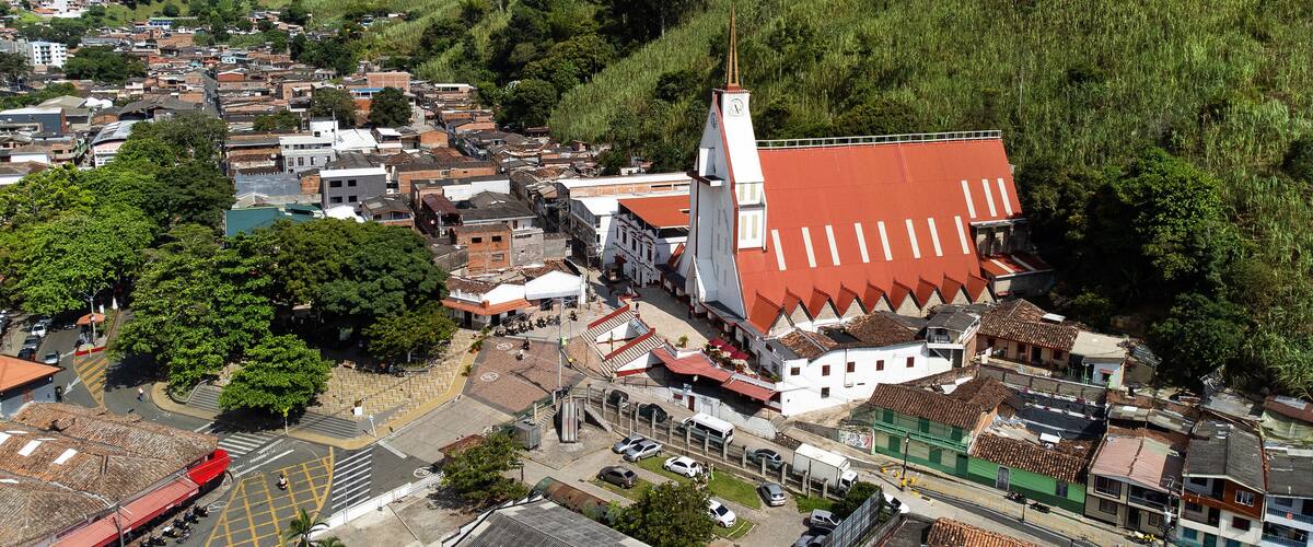 A town with a prominent church featuring a clock tower, surrounded by lush green hills and a mix of traditional and modern buildings.