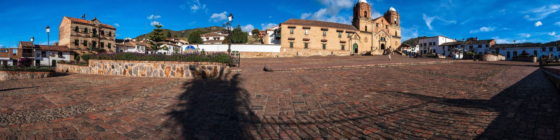 A historic plaza with cobblestone streets, a prominent church with two towers, and surrounding buildings.