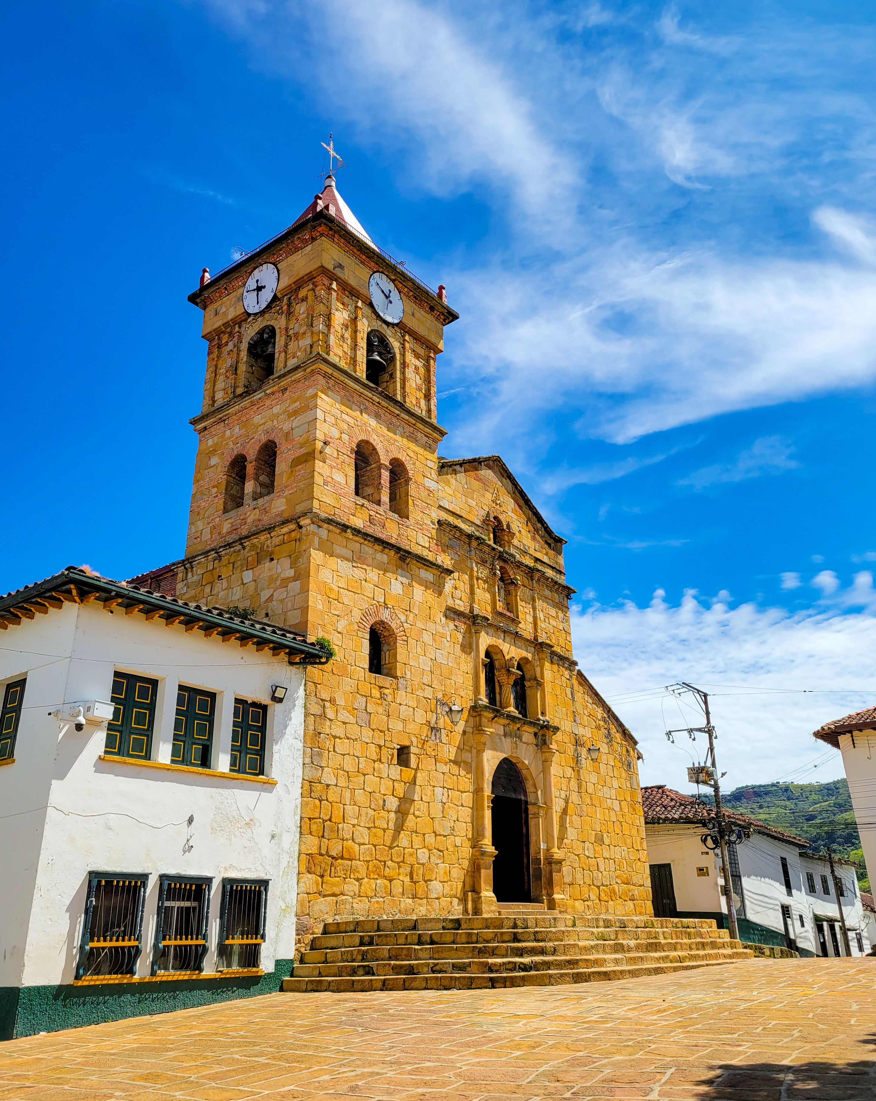 A historic stone church with a bell tower and a clock, set against a clear blue sky.