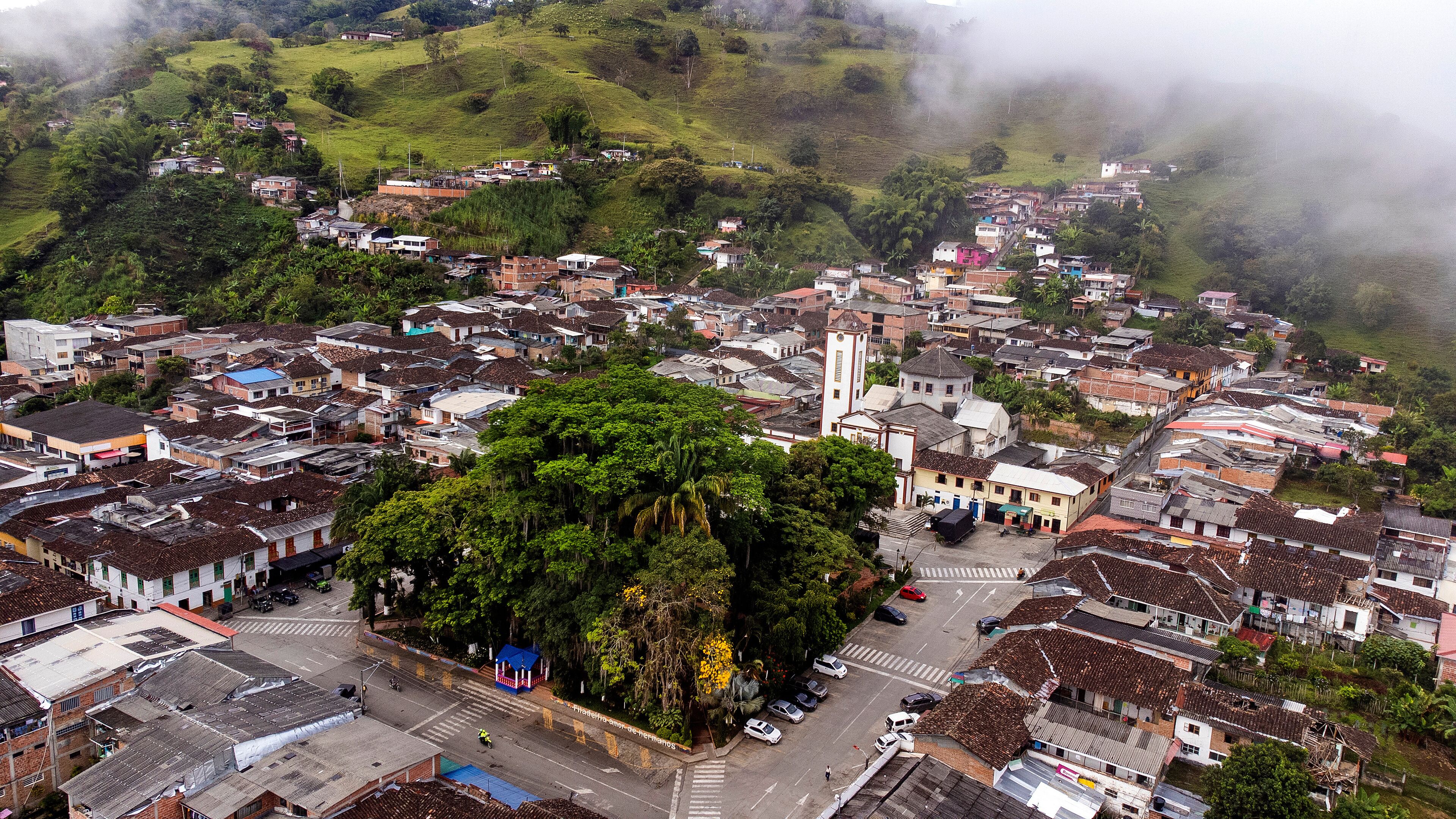 A town with a central plaza surrounded by buildings, a prominent church, and lush greenery.