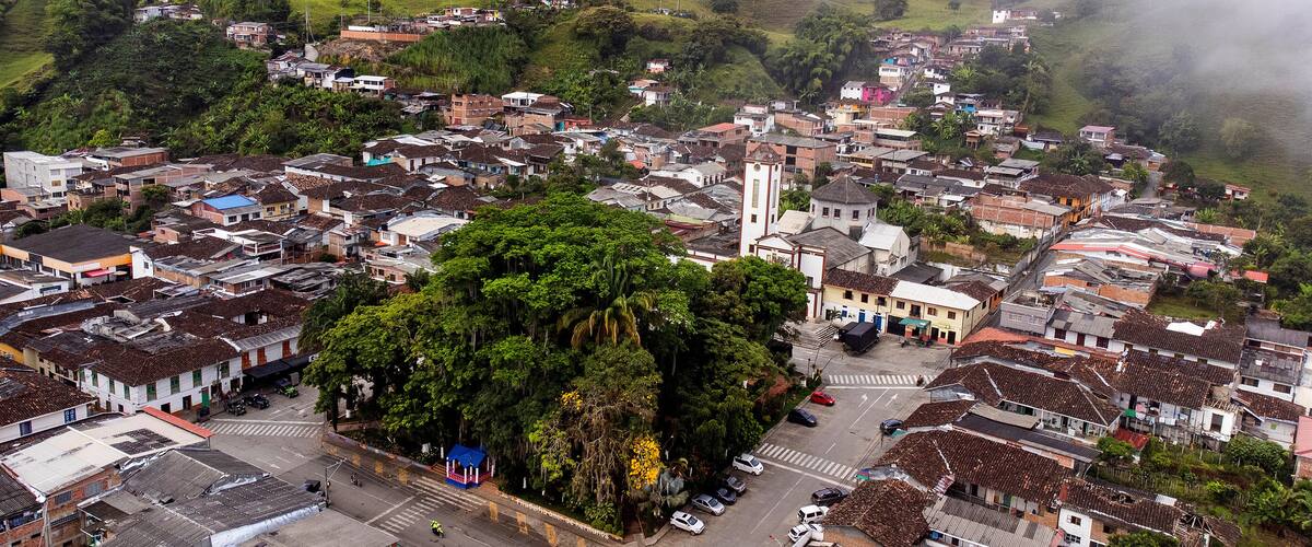 A town with a central plaza surrounded by buildings, a prominent church, and lush greenery.