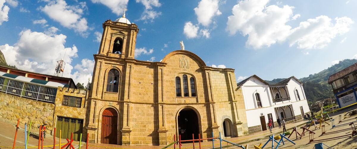 A historic church with a bell tower and arched windows, surrounded by a mountainous landscape.