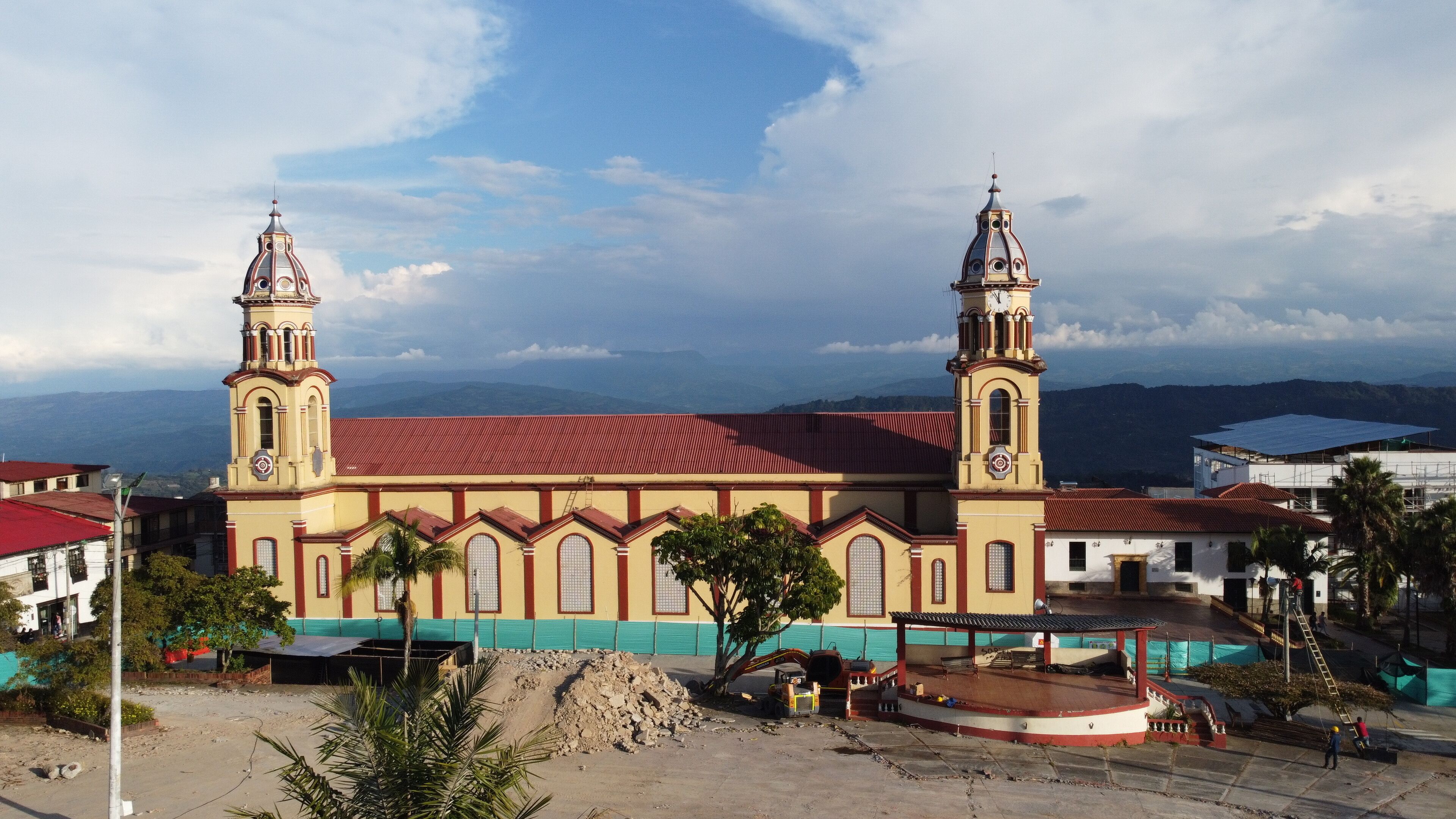 A church with two towers and a red roof, surrounded by construction and palm trees.
