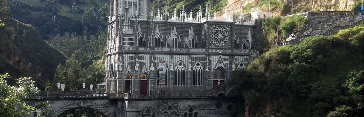 Una iglesia de estilo gótico con una aguja alta, un puente y abundante vegetación.