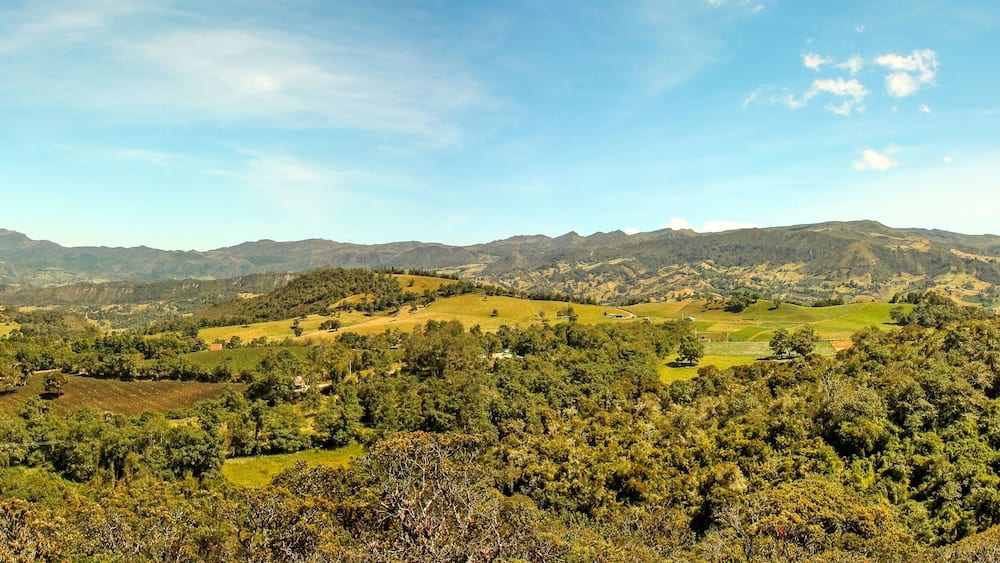 A mountainous landscape with rolling hills, dense forests, and scattered buildings.