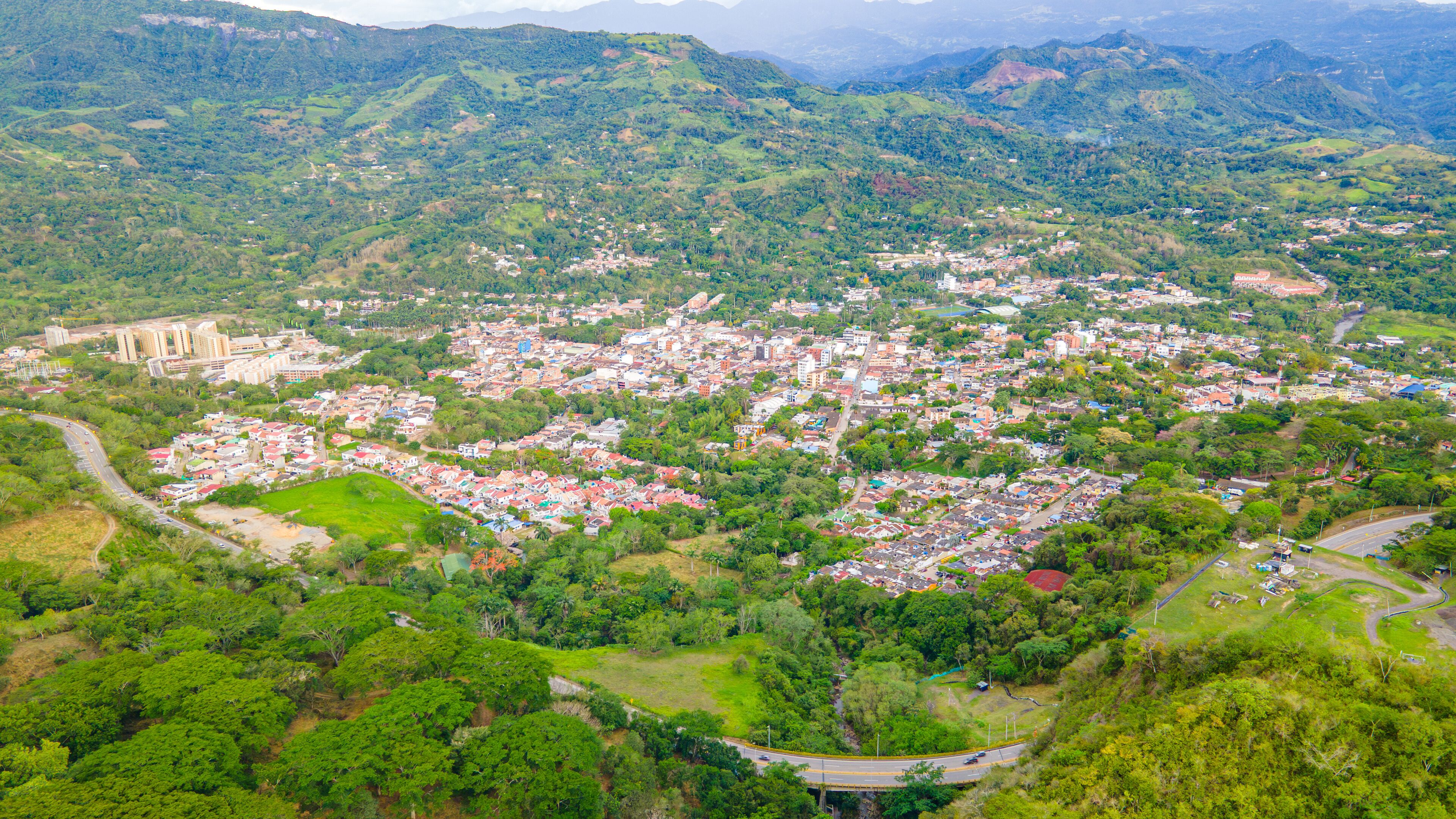 A densely populated town nestled in a mountainous region with lush greenery and a prominent church.