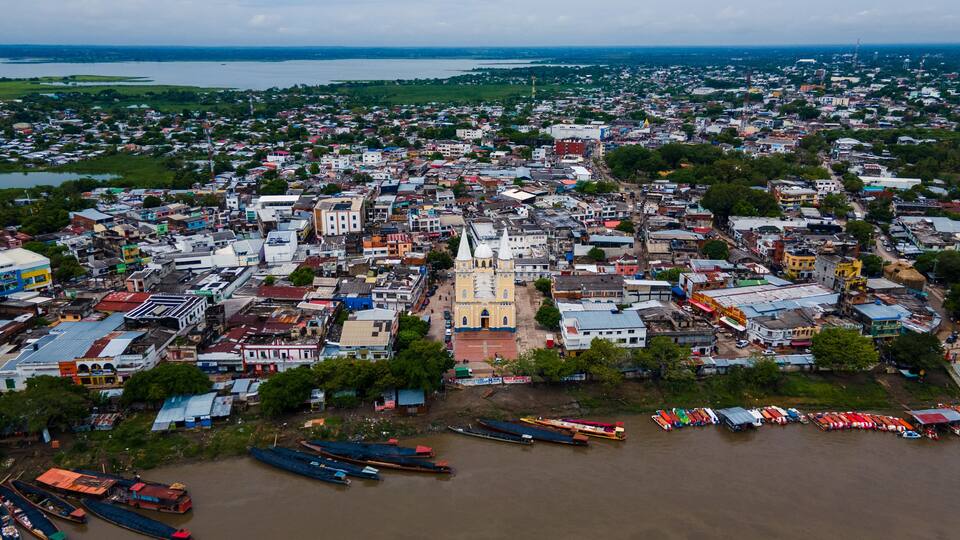 An aerial view of a city with a prominent church, dense housing, and a river with boats.