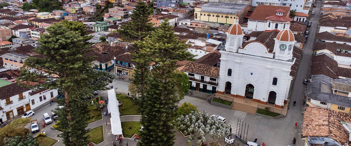 A town with a prominent white church with a dome, surrounded by residential buildings and a central plaza with a fountain.
