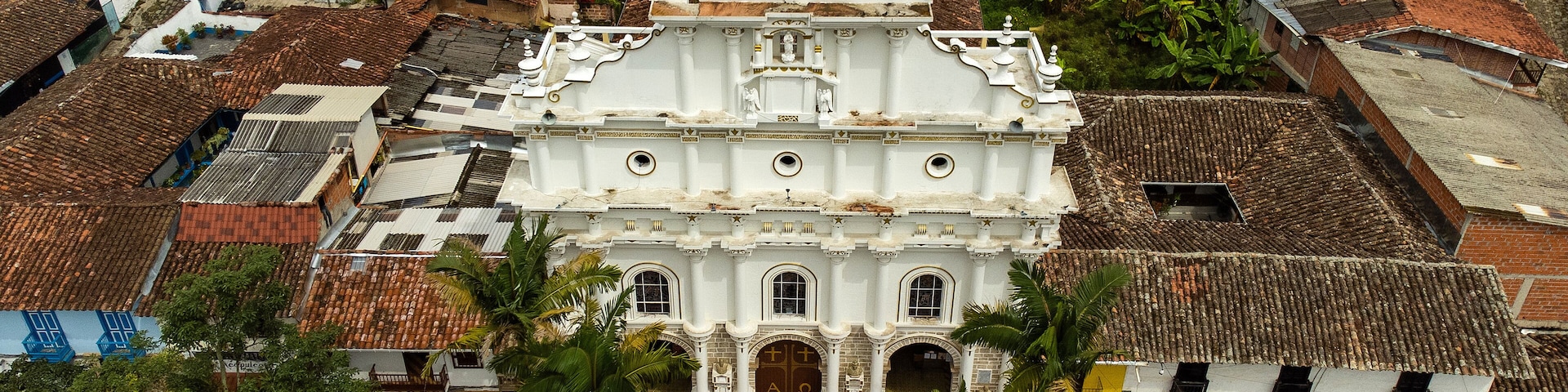 Vista aérea de una iglesia histórica con una torre del reloj, rodeada de edificios residenciales y palmeras.