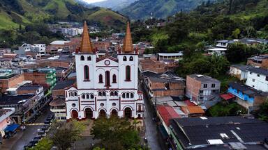 A white church with two towers, surrounded by residential buildings and lush green hills.