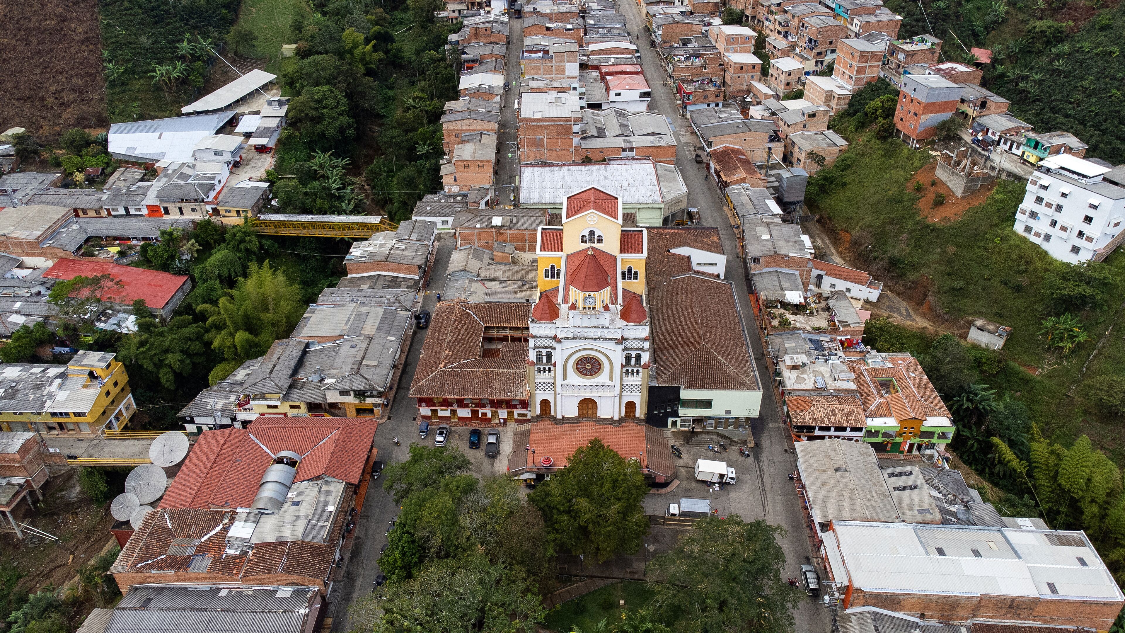 An aerial view of a town with a prominent church featuring a red roof and white walls, surrounded by residential buildings with red and grey roofs.