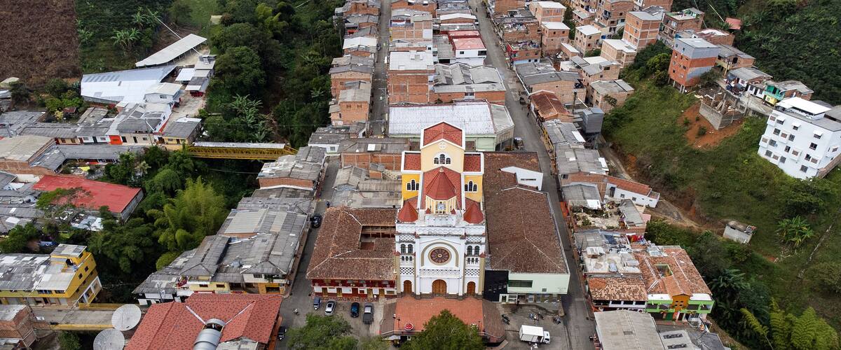 An aerial view of a town with a prominent church featuring a red roof and white walls, surrounded by residential buildings with red and grey roofs.