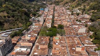 An aerial view of a densely packed urban area with terracotta-roofed buildings, a prominent church, and a train track running through the center.