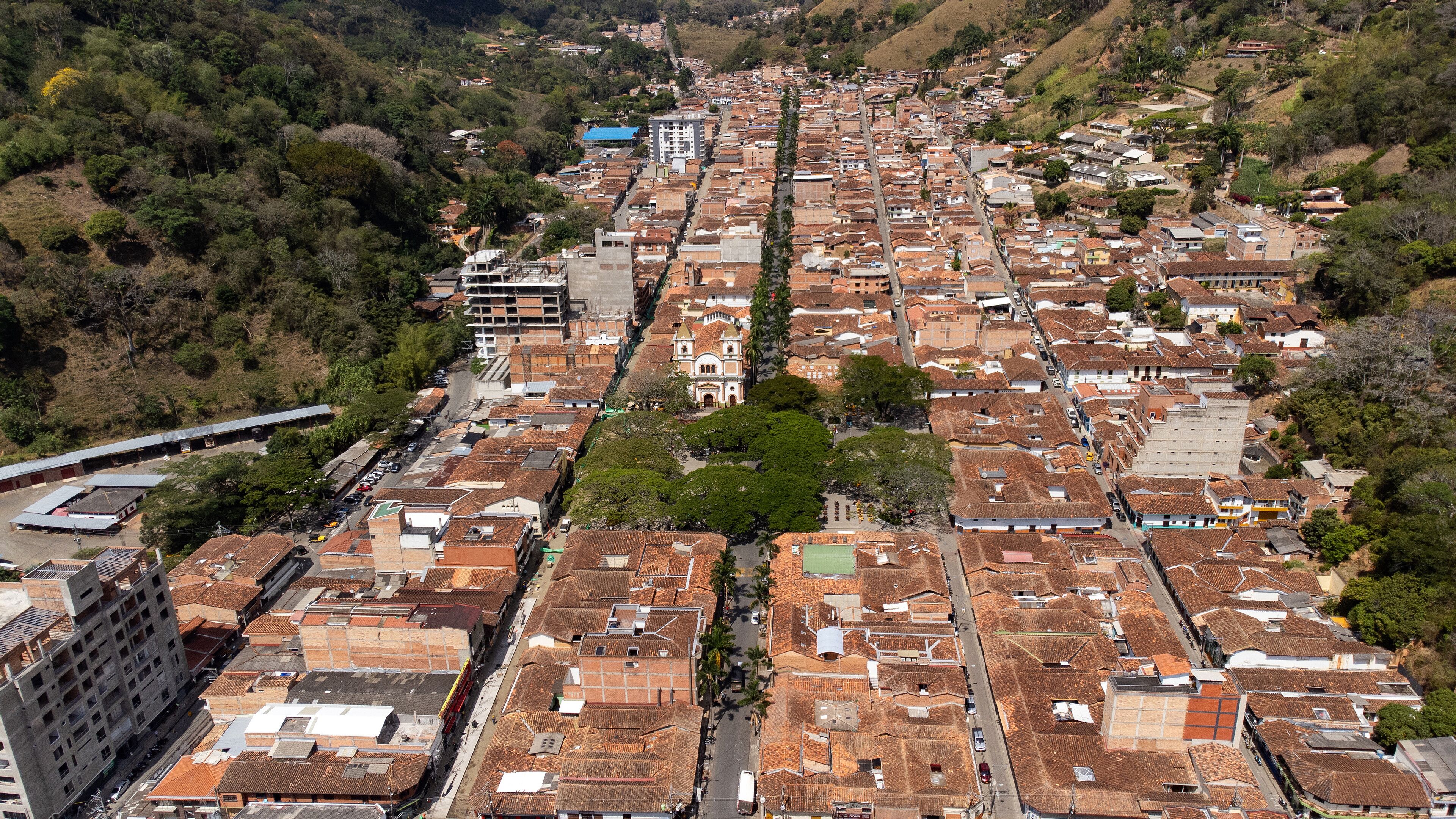 An aerial view of a densely packed urban area with terracotta-roofed buildings, a prominent church, and a train track running through the center.