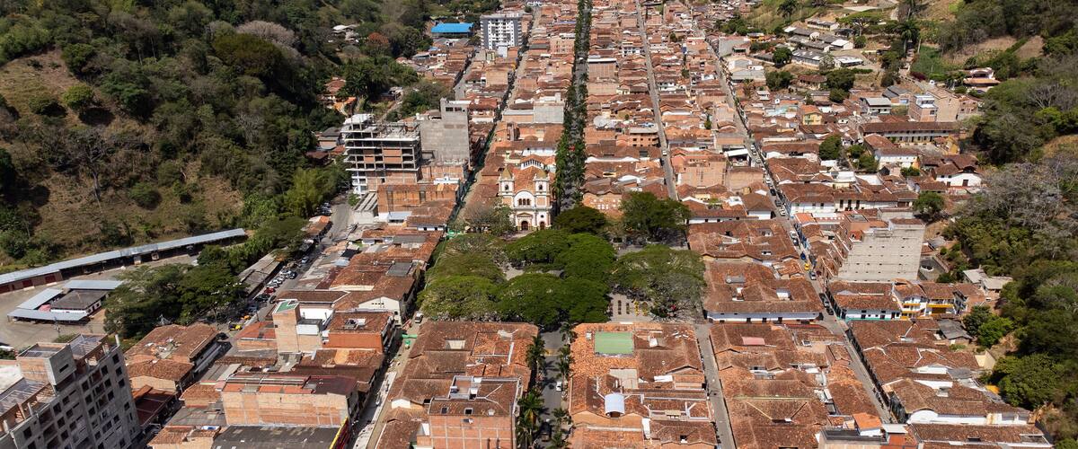 An aerial view of a densely packed urban area with terracotta-roofed buildings, a prominent church, and a train track running through the center.