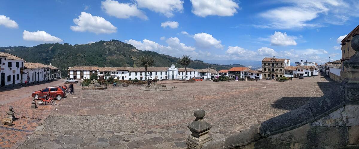 A cobblestone plaza with historic buildings, a mountain backdrop, and a clear sky.