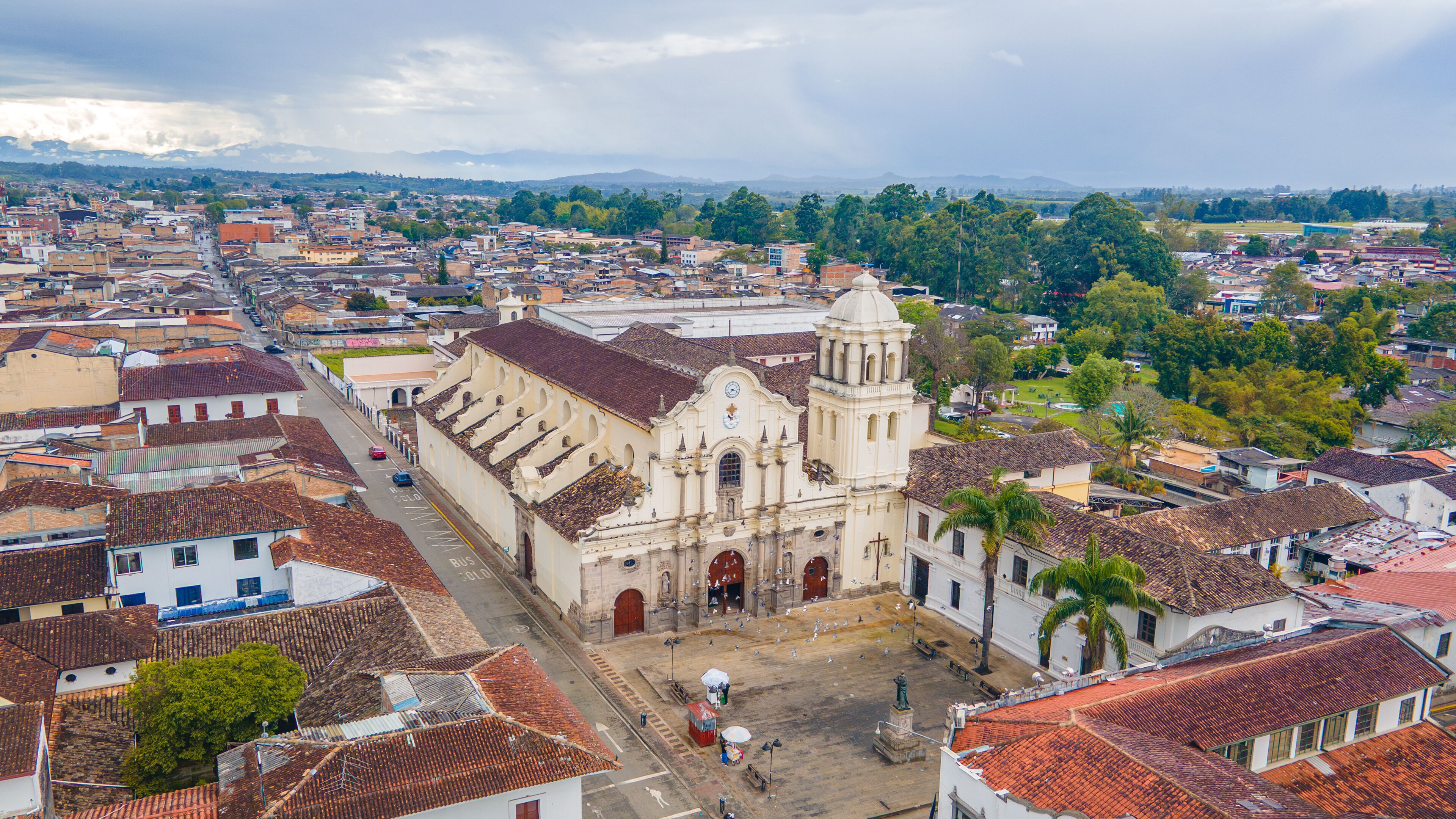 A historic church with a dome and bell tower, surrounded by a cityscape with red-tiled roofs and greenery.