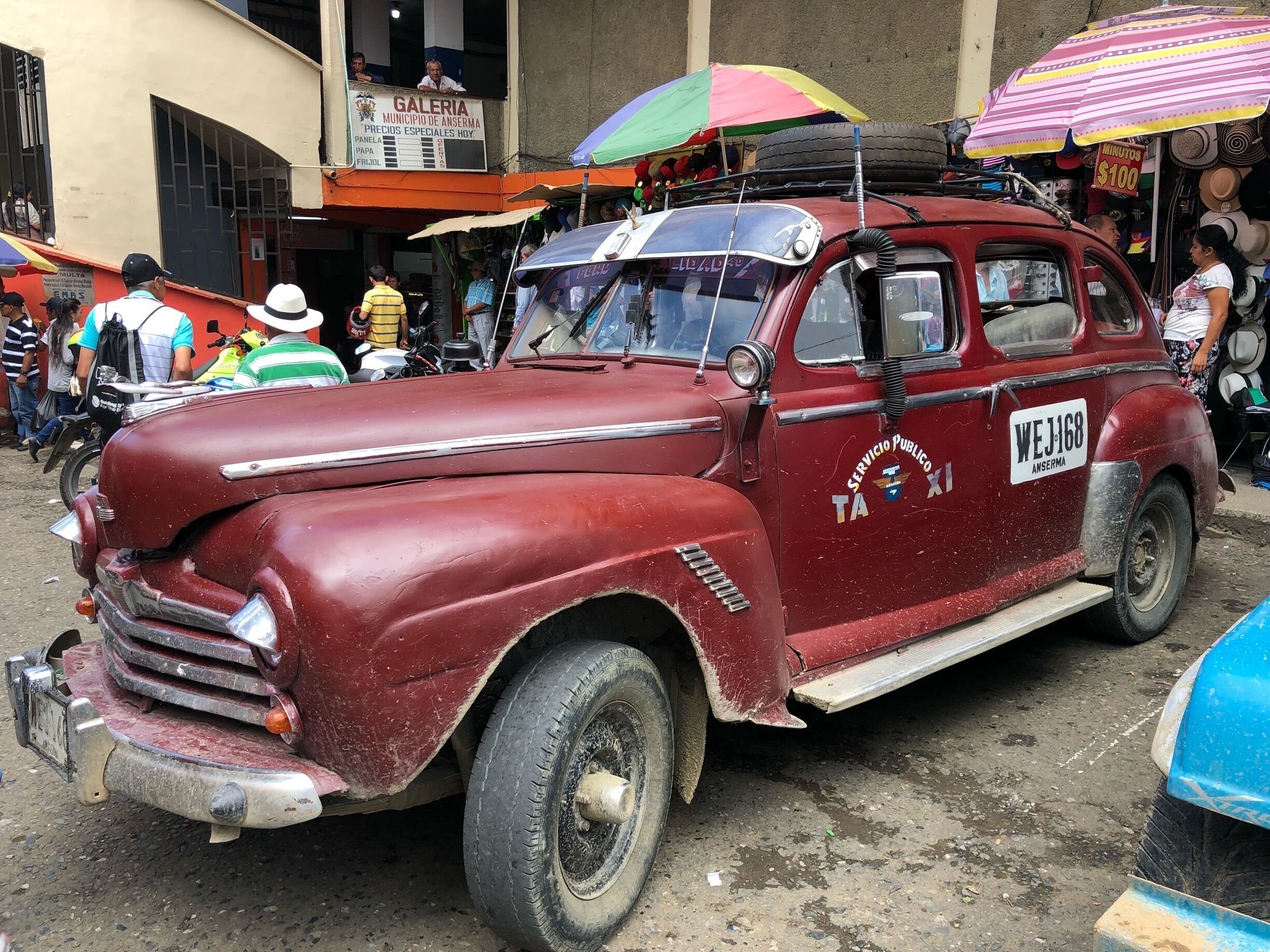 A vintage red car with "Servicio Publico" and "Taxima" on its side parked in a busy street.