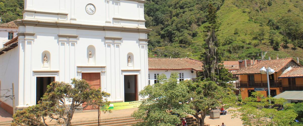 A white church with a bell tower, surrounded by trees and a hillside.