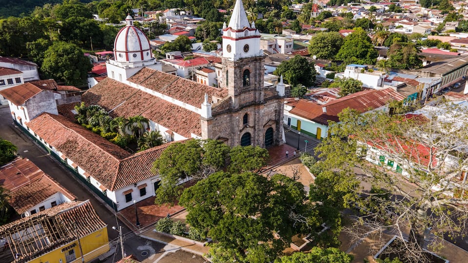 A historic town with a prominent church featuring a bell tower and dome, surrounded by lush greenery and residential buildings.