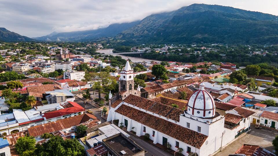 A historic town with a prominent church featuring a dome and bell tower, surrounded by lush greenery and a river.