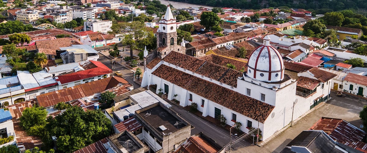 A historic town with a prominent church featuring a dome and bell tower, surrounded by lush greenery and a river.