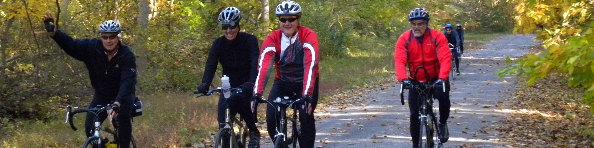 Tres ciclistas en un camino pavimentado rodeado de árboles con hojas otoñales.