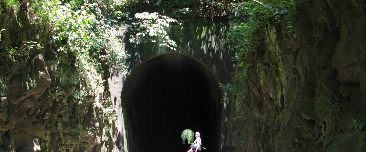 A person riding a bicycle through a tunnel surrounded by rocky cliffs and greenery.