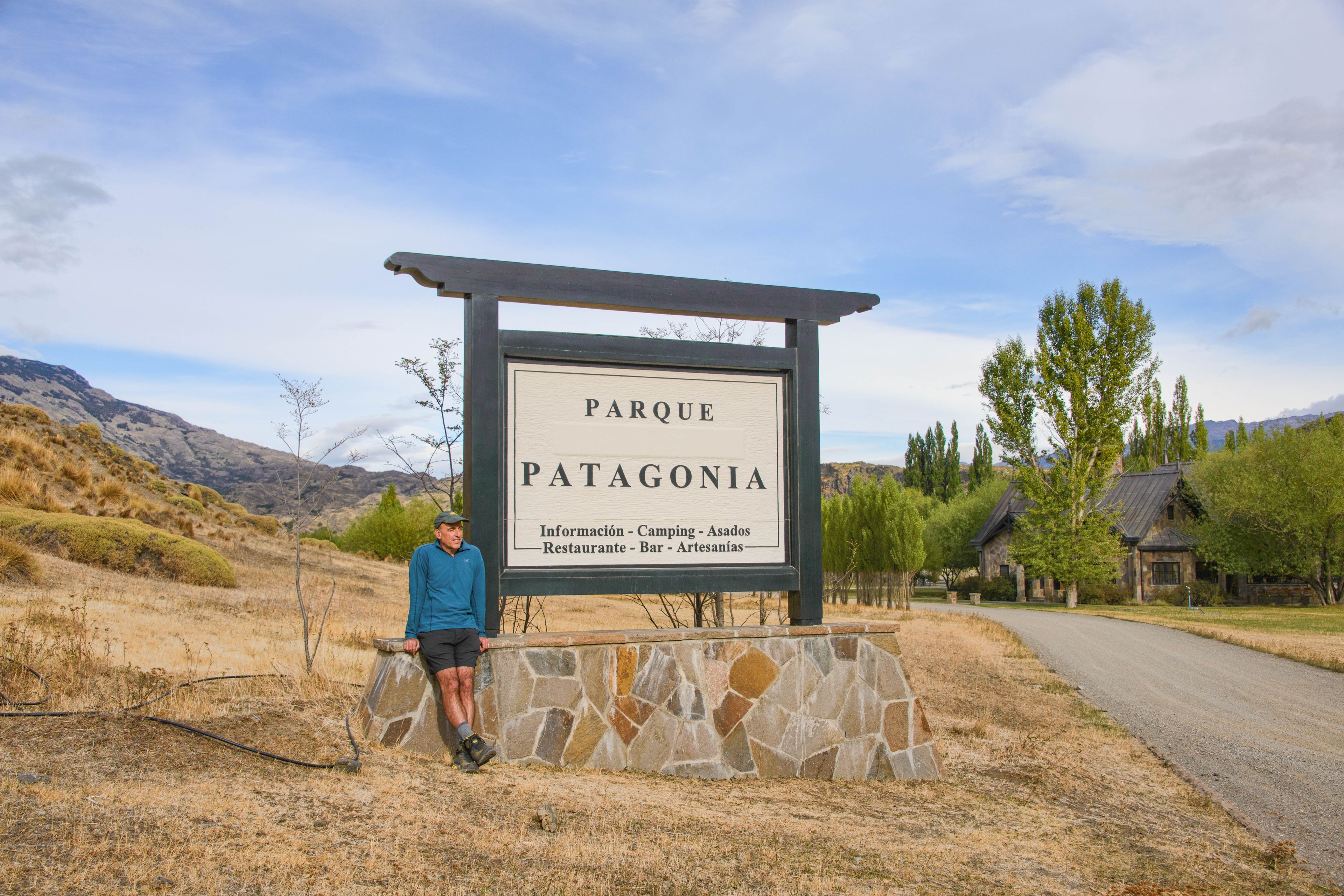 A sign for a park named 'Patagonia' with a stone wall and a person standing beside it.