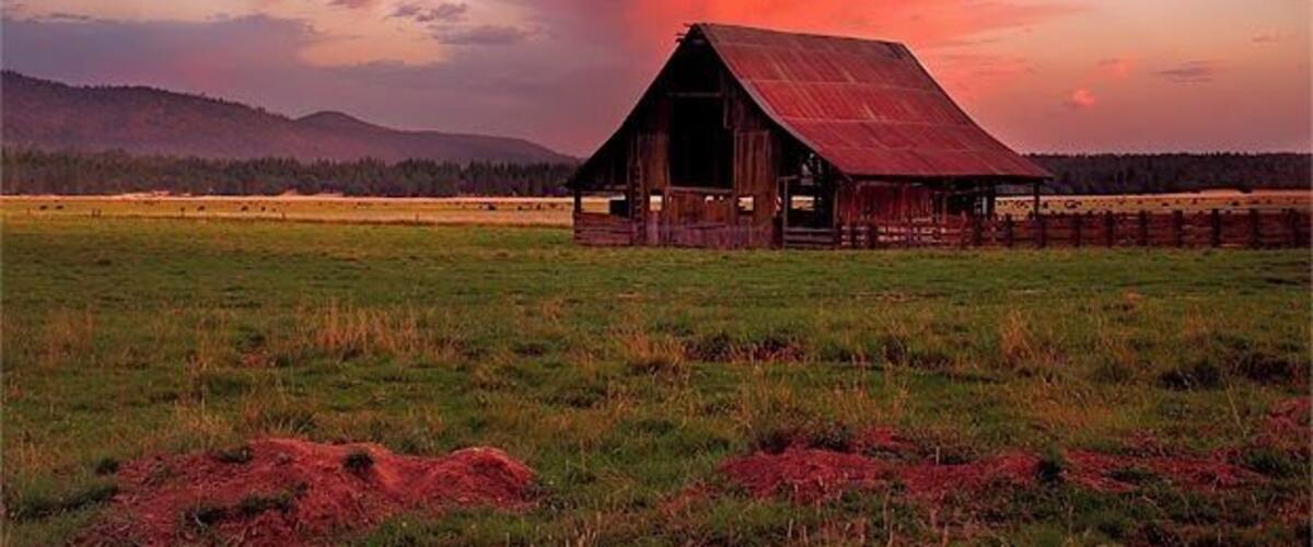 A barn in a field with a colorful sunset sky.
