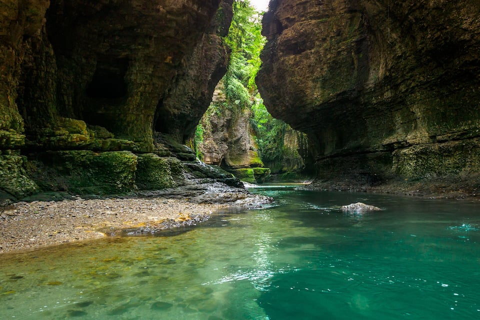 Ein klarer, türkisener Fluss fließt durch eine felsige Schlucht mit moosbewachsenen Wänden.