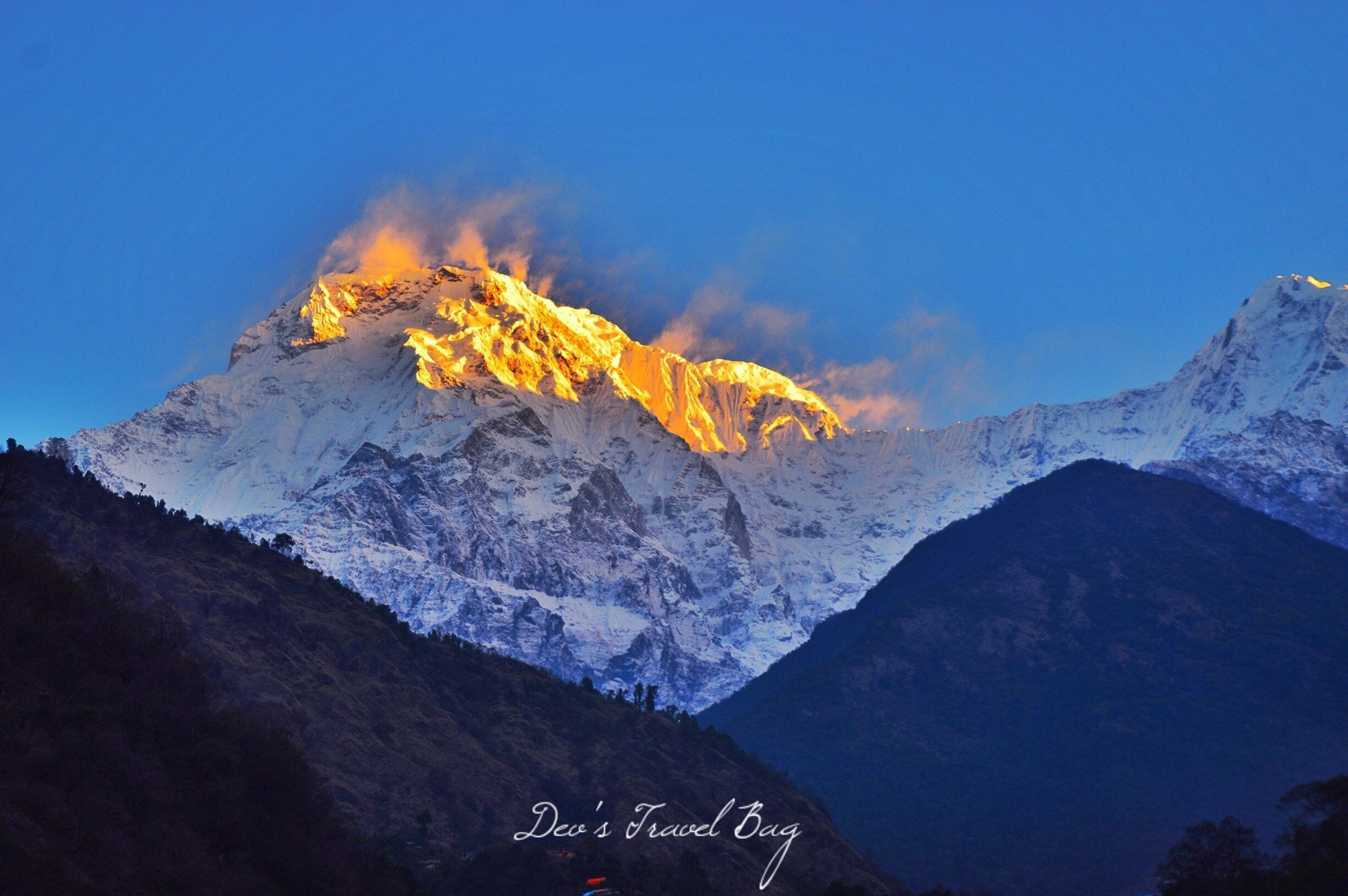 A snow-covered mountain range with a peak illuminated by sunlight.