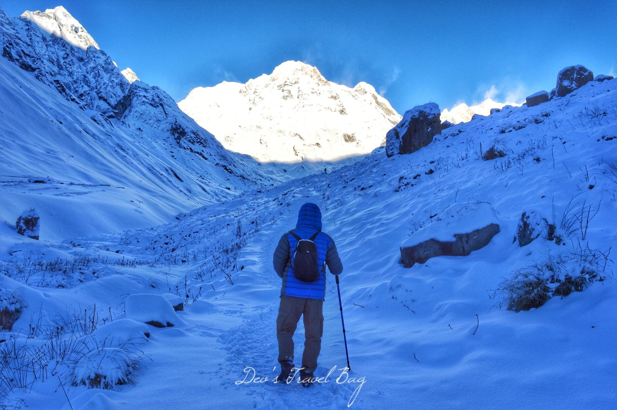 A hiker in a snowy mountainous landscape with a clear sky.