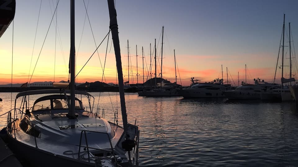 Un puerto deportivo con varios veleros amarrados al atardecer.