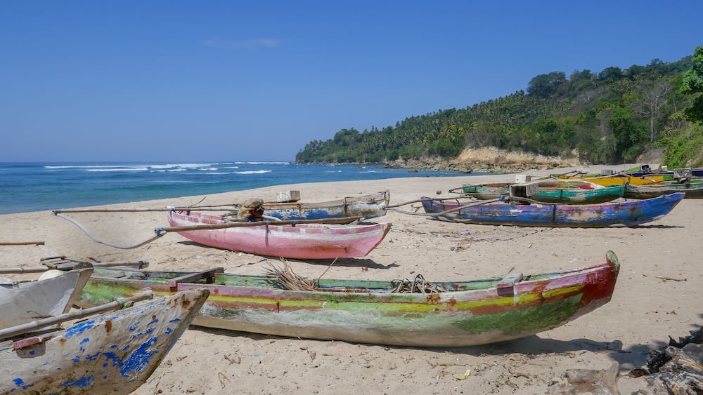 A beach with several colorful boats and a forested hillside in the background.