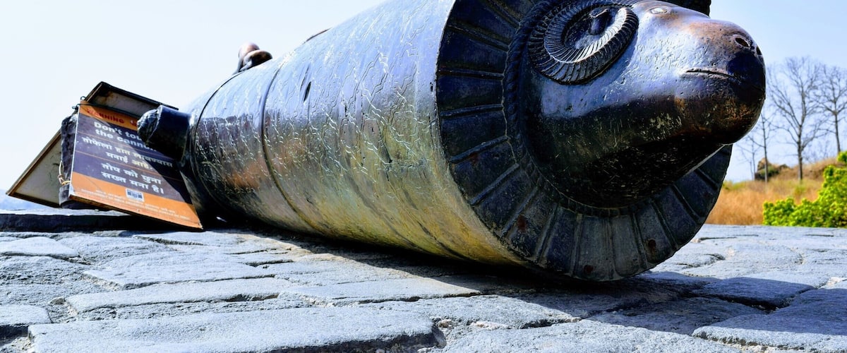 A large, metallic sculpture resembling a head with a circular eye and a nose, lying on stone pavement.