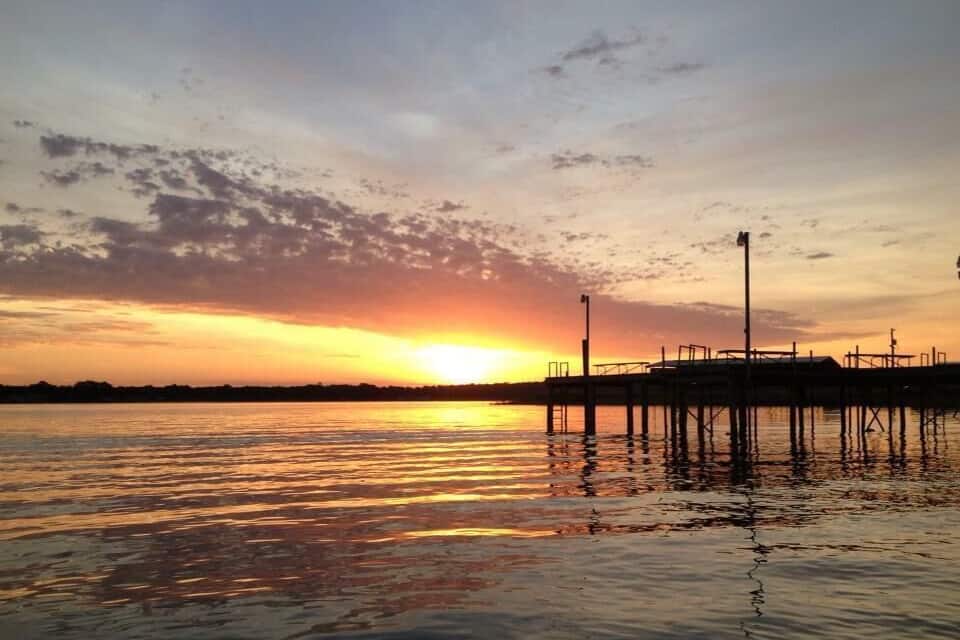 A sunset over a calm body of water with a pier extending into the water.