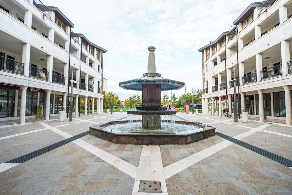 A central fountain in a plaza surrounded by multi-story buildings with balconies.