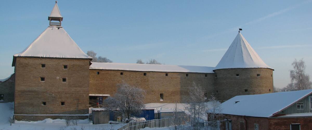 A snow-covered brick building with two towers and a small adjacent structure.
