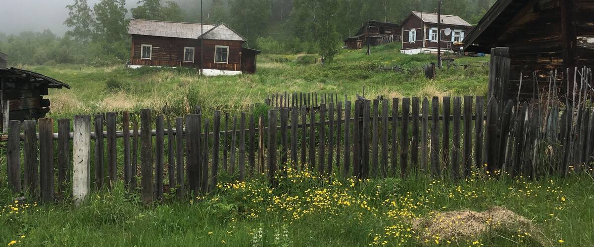 A foggy rural landscape with wooden houses and a wooden fence.
