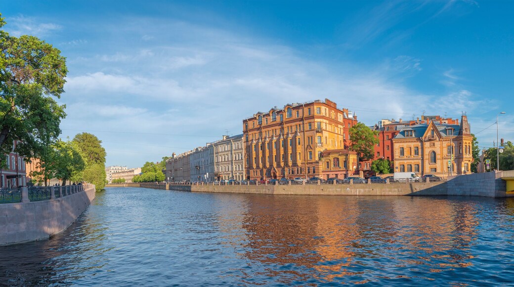A river with buildings on the opposite bank, a bridge, and a clear sky.