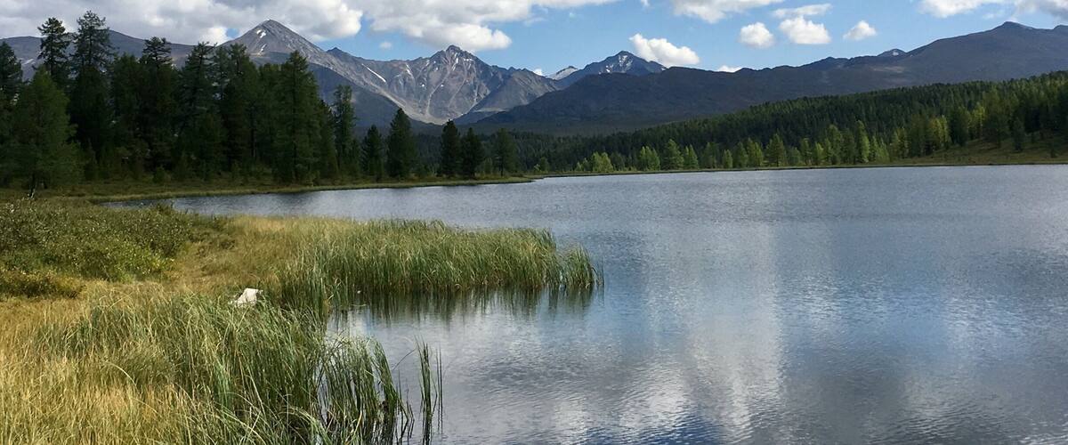 A lake surrounded by mountains and dense forests under a partly cloudy sky.