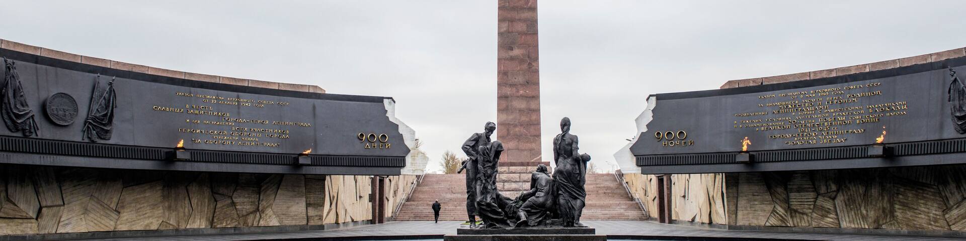 A monument with inscriptions and statues, surrounded by a cobblestone plaza.